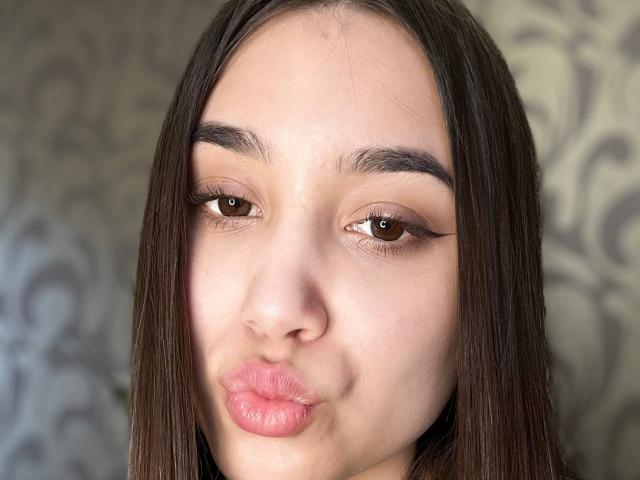 ShawneeLinderholm's face, brown eyes, straight brown hair, full pink lips puckered, subtle makeup, clear skin, slightly arched eyebrows, soft natural light, slightly tanned skin, gentle expression.