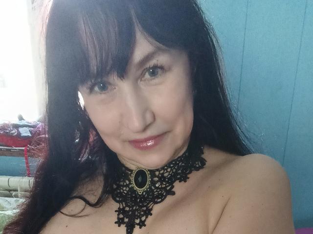 Mila69, con i capelli scuri, indossa un collare di pizzo nero, ha labbra rosa lucide ed è senza top, mostrando il seno. Ha gli occhi azzurri e un leggero sorriso..