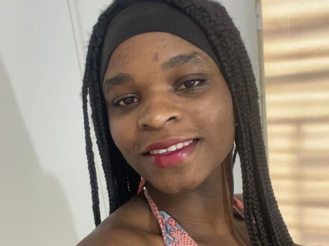 RenataWalker with dark braids, black headband, nose ring, and pink lipstick, smiling with shiny pink lips, showing off her medium brown skin and small, cute nose.