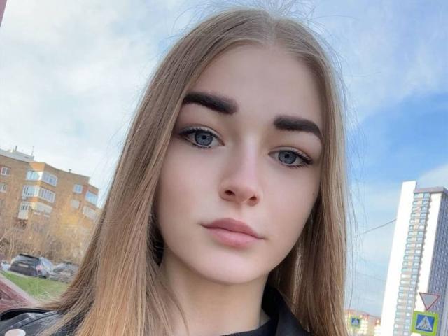 CarolannFettig has blue eyes, full pink lips, and long straight blonde hair, wearing a black leather jacket, with slightly raised eyebrows and a neutral expression.