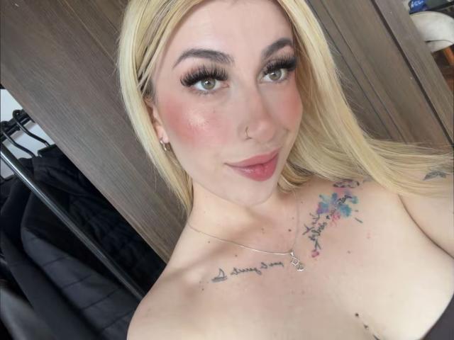SammyViolet has blonde hair, green eyes, and a cute smile. She's topless with tattoos on her chest, including "don't worry" and colorful star designs. She's got big tits.
