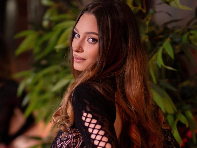 AlexaWillis has long brown hair, a nose ring, and a sexy smile, looking back over her shoulder in a black, mesh-top dress, showing her tits through the pattern.
