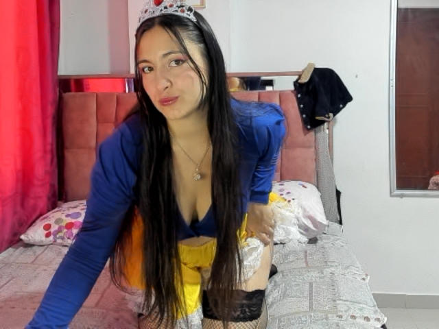 VenusSweetPalmer, long black hair, blue top, yellow skirt, black lace thigh-highs, tiara, kneeling on bed, cleavage, small breasts, cute, bedroom, red curtain, mirror, clothes on wall.