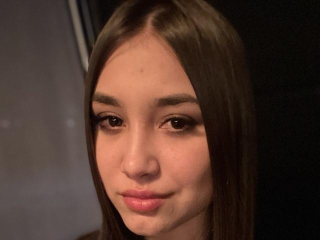 ShawneeLinderholm has straight brown hair, brown eyes, and pink lips with a slight smile. Her skin is fair, and she has minimal makeup. She looks cute.