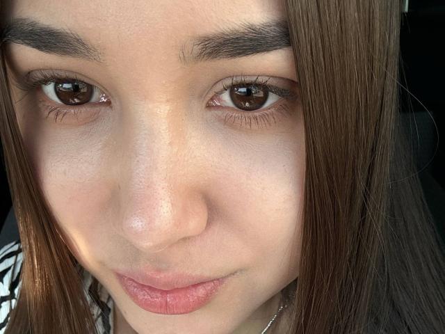 ShawneeLinderholm's face, brown eyes, slightly parted pink lips, straight brown hair, light skin, small nose, thin eyebrows, subtle makeup, small silver necklace, close-up, soft light.