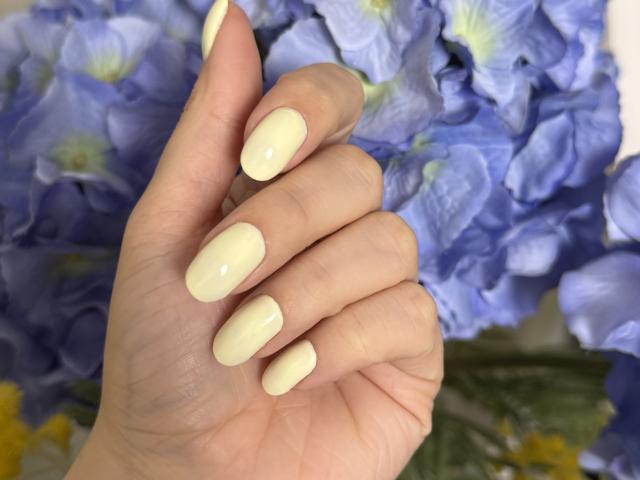 KarKutie's hand with pale, glossy, almond-shaped nails, holding a cluster of blue flowers. Her skin is light, and her fingers are slightly curled.