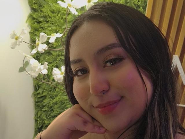 SalomettX, con cabello oscuro, aro en la nariz y delineador de ojos, sonriendo suavemente, con el mentón apoyado en la mano, usando un rubor rosa discreto, mirando a la cámara..