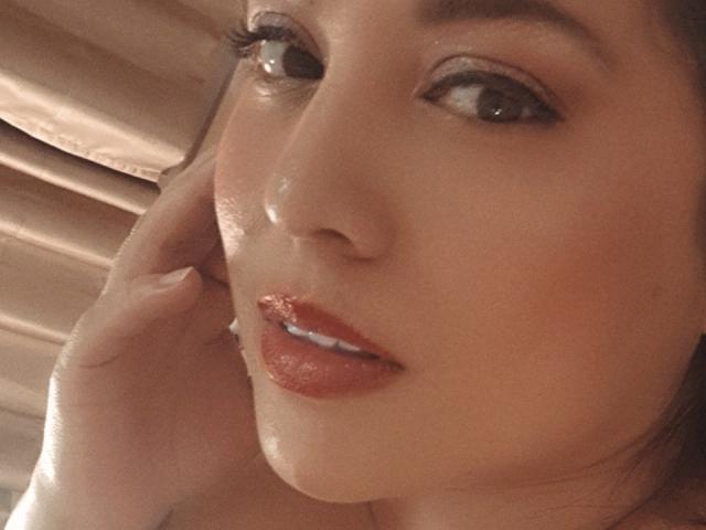 PaulaAnd's face, slightly flushed, with glossy red lips and brown eyes looking to the side. Her hand touches her cheek, showing a cute, sexy, and attractive look.