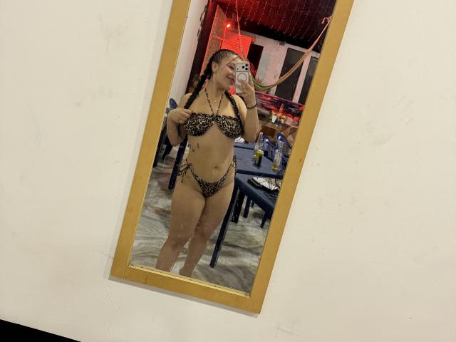LorensDouce in a leopard-print bikini, showing her tits and ass, taking a mirror selfie with her phone, standing in a room with a table and drinks.