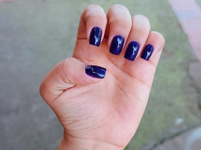 Genesiss's hand with shiny, dark blue, glossy-nail polish on all fingers, showing a slight reflection. Her fingers are slightly curled. Her skin is light and smooth.