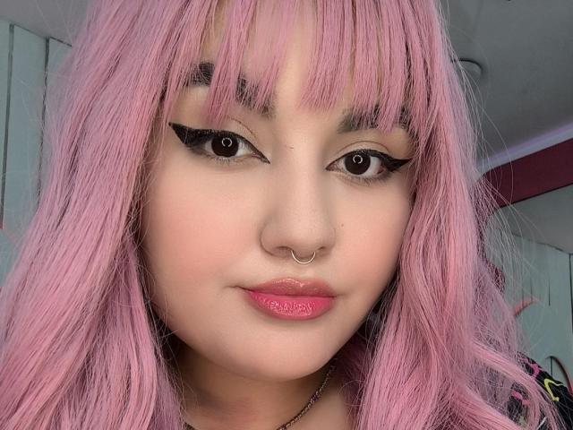 MarlaBriard has pink hair, black winged eyeliner, pink lipstick, and a nose ring. Her face is centered, showing a cute, slightly smug expression. Her eyes are looking directly at the camera.