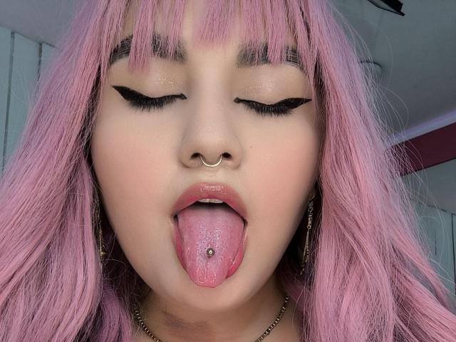 MarlaBriard has pink hair, a nose ring, and a tongue piercing with a ball on it. Her eyes are closed with black winged eyeliner, and her tongue is out.