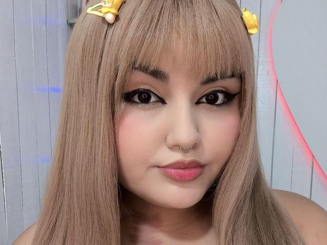 MarlaBriard has blonde hair with yellow hair clips, thick black eyeliner, pink lipstick, and a nose ring. Her face is centered in the photo.
