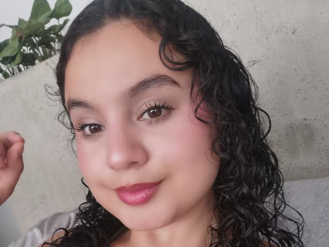 TaniaRichmond has curly black hair, brown eyes, and pink lipstick, with a subtle smile and fair skin, looking at the camera with a relaxed, cute expression.