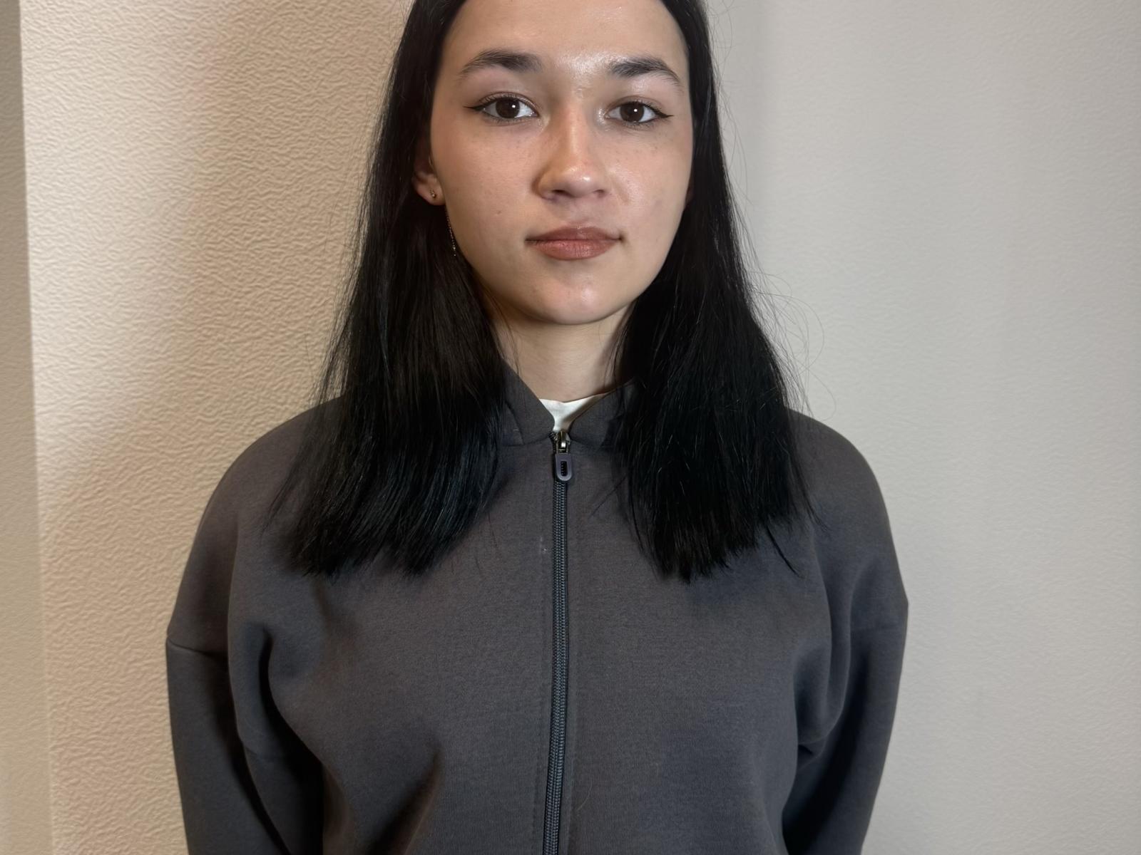 KaceyKuney has straight black hair, brown eyes, and a neutral expression. She's wearing a dark gray zip-up hoodie. Her ass is not visible. Her tits are small.