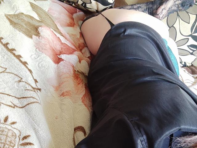 MinistraX's black thong is visible, showing her pale, round ass. She's lying on a floral blanket, wearing black lace stockings and black leather boots. Her blue underwear is partially seen.