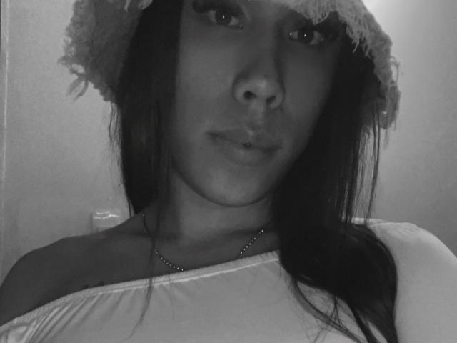 GeraldineSuan's face in a black-and-white selfie, wearing a lace hat, off-shoulder top, and necklace, with long dark hair and subtle pout, showing small tits.
