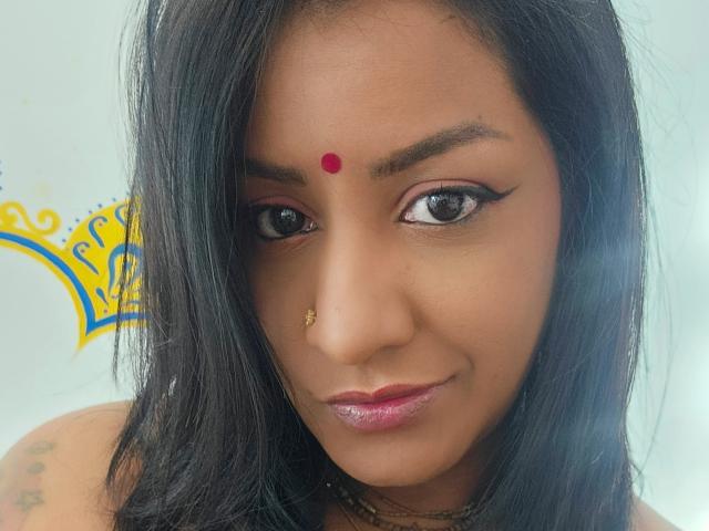 Nahirr has dark brown skin, black straight hair, a red bindi on her forehead, and a gold nose ring. She's smiling with pink lipstick, black eyeliner, and tattoo on shoulder.