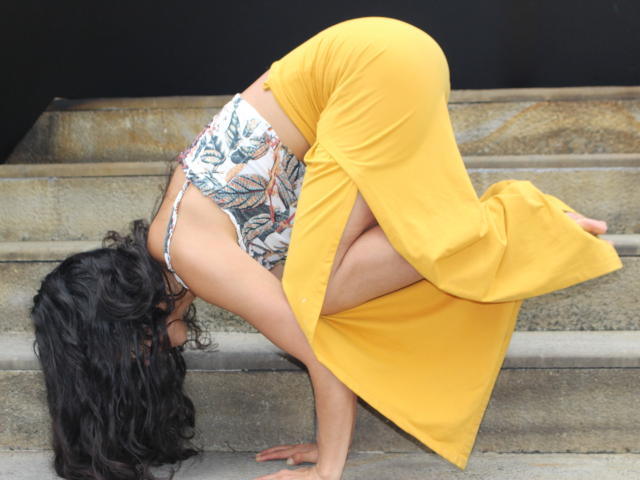 LucyySky is bent over, wearing a yellow skirt and floral top, exposing her tits and showing her ass. Her curly black hair is down, hands on stairs.
