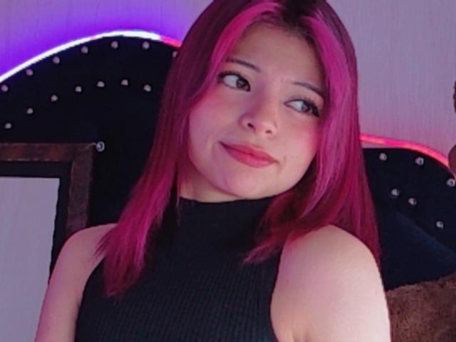 ShofiaWett tiene el cabello rosa, un cuello alto negro y una sonrisa encantadora. Está mirando hacia un lado, con un maquillaje sutil y una vibra relajada y sensual..