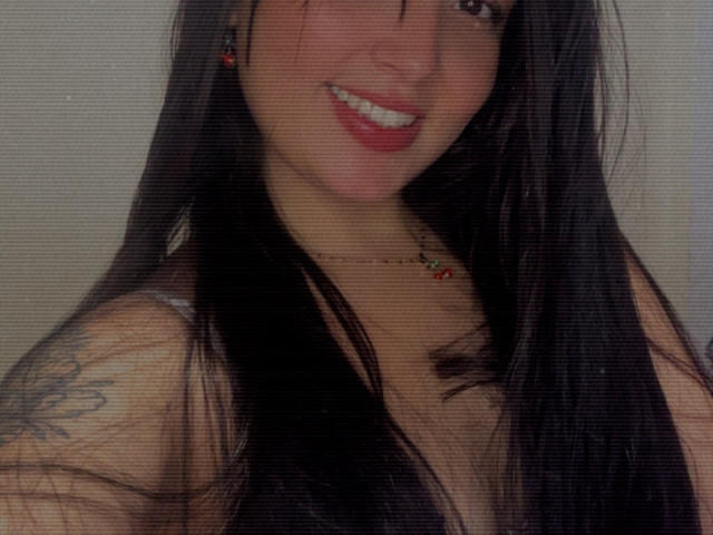 SarahGood with long black hair, smiling, showing teeth, red lipstick, small red earrings, necklace, tattoo on left shoulder, wearing a sleeveless top, upper body shot, grid effect.