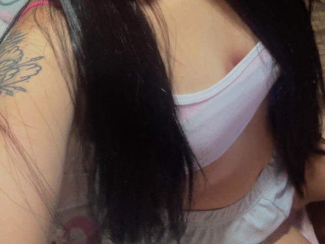 SarahGood's white bra, showing a sliver of her small tit, with black hair covering her chest. A tattoo on her right shoulder is partially visible.