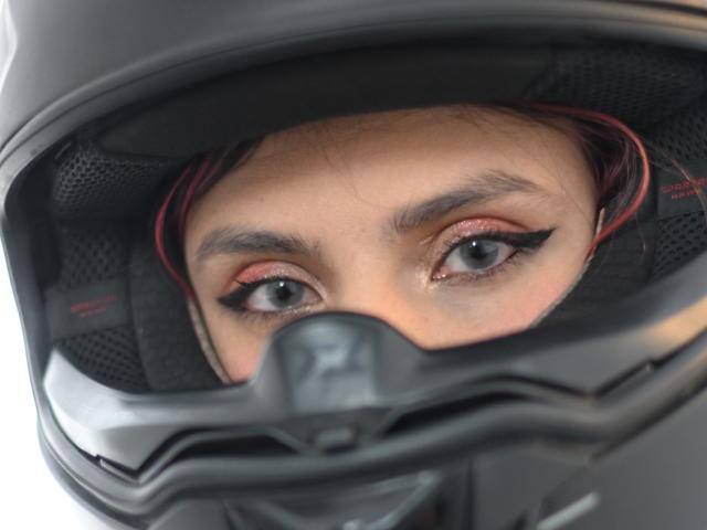 TifanySuarez's eyes, looking through a black motorcycle helmet, with red accents and black eyeliner, showing intense, focused expression. Her eyebrows are slightly raised.