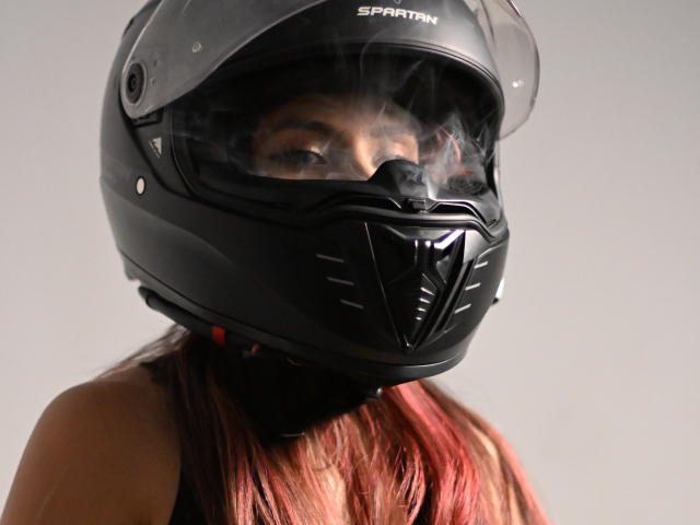TifanySuarez wearing a black Spartan helmet with a clear visor, steam rising from her breath, black mask covering her nose, and red-tinted hair visible.