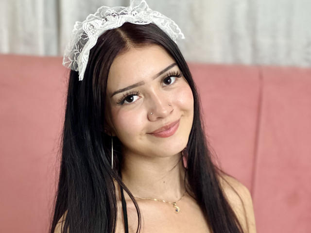 KarinaCurvy with long black hair, wearing a white lace headband, smiling with a nose ring, and a necklace, showing her cute face and small tits.