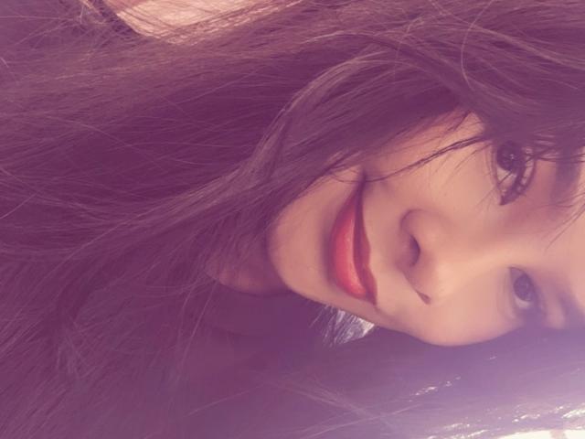 Yurimy's face with long, dark brown hair covering one eye, smiling with red lipstick, and a slight nose tilt. Her eyes are slightly open, and she's looking forward.