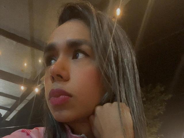 Iria's face, brown skin, long straight brown hair, pink lipstick, thoughtful expression, hand on neck, warm yellow fairy lights, soft focus, slight bokeh effect, casual night selfie.
