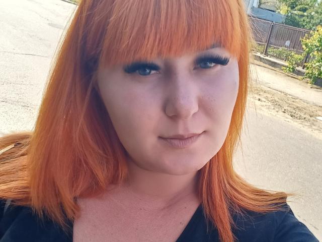 Kirobra69 tiene el cabello de un naranja brillante, ojos azules, y lleva delineador de ojos negro con pestañas largas. Está mirando a la cámara con una sonrisa leve y segura..