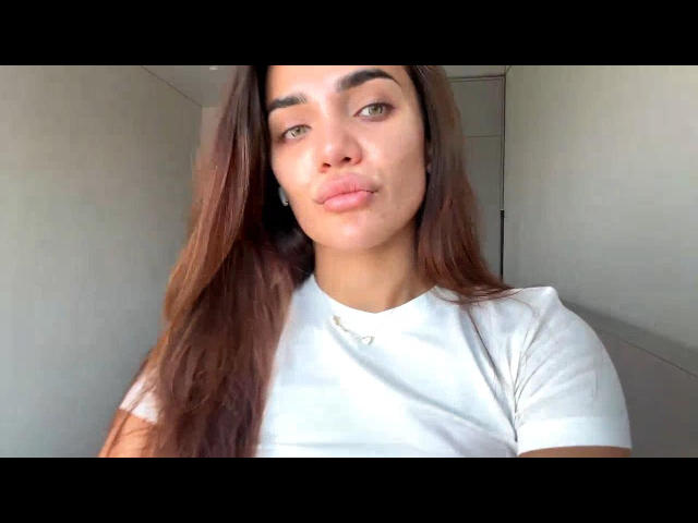 ArdithKounick with long brown hair, wearing a white shirt, has pouty pink lips, and is looking at the camera with slightly raised eyebrows. She has small tits and a cute face.