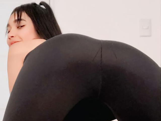 YayaLm has black puffy pants on, showing her big ass. She's bent over, looking back with a slight smile, and has black hair in a ponytail.