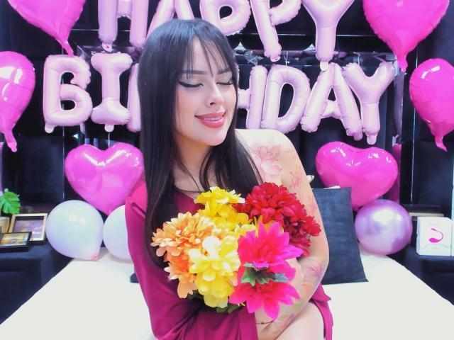 AlisonTatcher with long black hair, red dress, holding colorful flower bouquet, smiling, tattoos on right arm, pink balloons, heart-shaped balloons, happy birthday, cute, sexy, attractive.
