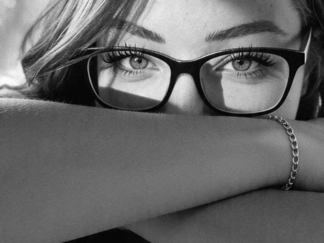 DirtyQueen – heiß, mit Brille, Arme verschränkt, intensiver Blick. Ihre Augen sind scharf, mit langen Wimpern, und sie trägt einen silbernen Armreif. Schwarz und weiß, sexy, ernst..