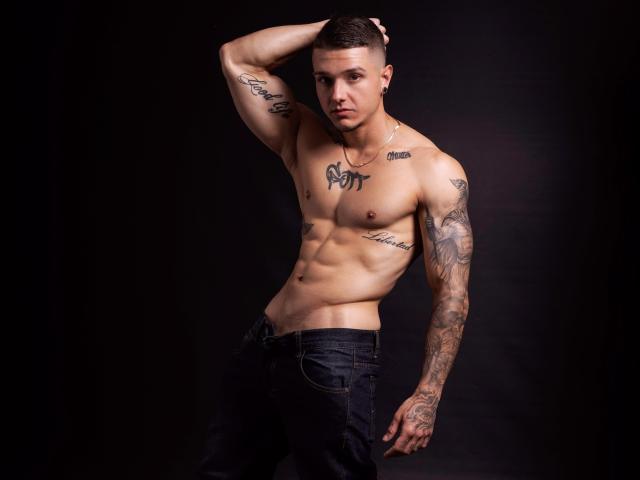 TysonRich, torse nu, musclé, avec des tatouages sur la poitrine et les bras, jean noir, cheveux bruns courts, une main dans les cheveux, expression sérieuse, fond noir, abdominaux visibles, tatouages sur la poitrine, tatouage sur le cou..