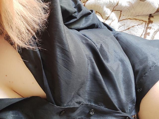 Il vestito nero di MinistraX è tirato su, rivelando una piccola parte del suo seno e un po' del suo sedere pallido e lentigginoso. I suoi capelli biondi sono a sinistra..