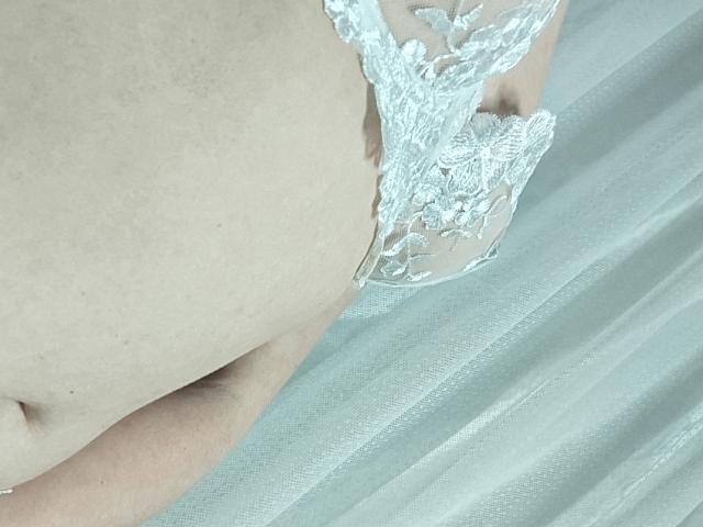 GladisBelle's pale skin with a slight belly, wearing white lace panties, showing her left ass cheek and a small part of her right thigh.