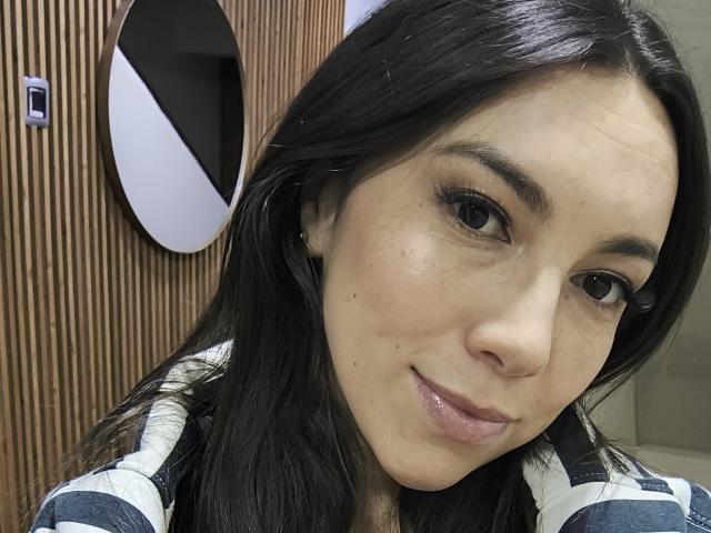 MiaReed has shiny black hair, dark eyes, and a slight smile, wearing a striped shirt. She's showing off her cute nose and subtle makeup. Boobs are not visible.