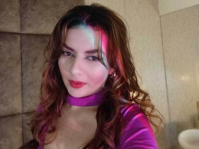 Zwart-wit foto van HanaGardinier met lang donker haar, die over haar schouder kijkt, waarbij haar blote schouder en bovenkant van haar borst zichtbaar zijn, haar lippen lichtjes open, in een subtiele, sexy pose..