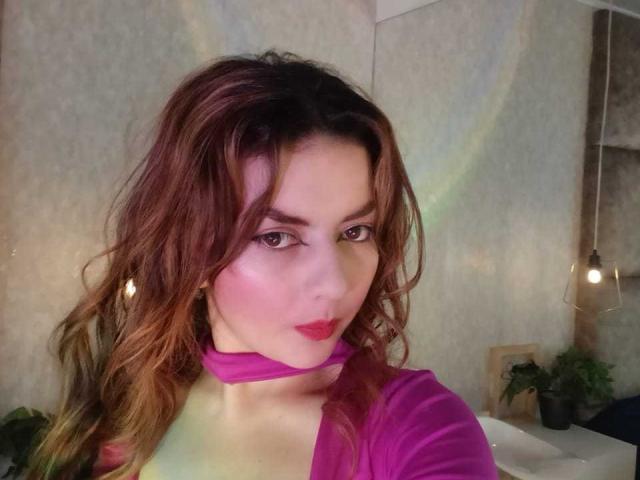 Zwart-wit selfie van HanaGardinier met lang donker haar, zwarte nagellak, een crop top die haar buikspieren laat zien, ze houdt een telefoon vast met een uitsparing voor de camera, en draagt een ketting..