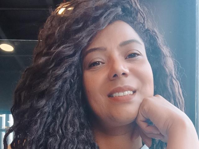 KenyaKarath tiene el pelo negro y rizado, ojos marrones y una ligera sonrisa, con el mentón apoyado en la mano y los dientes a la vista. Su piel es de color marrón medio y es muy linda..