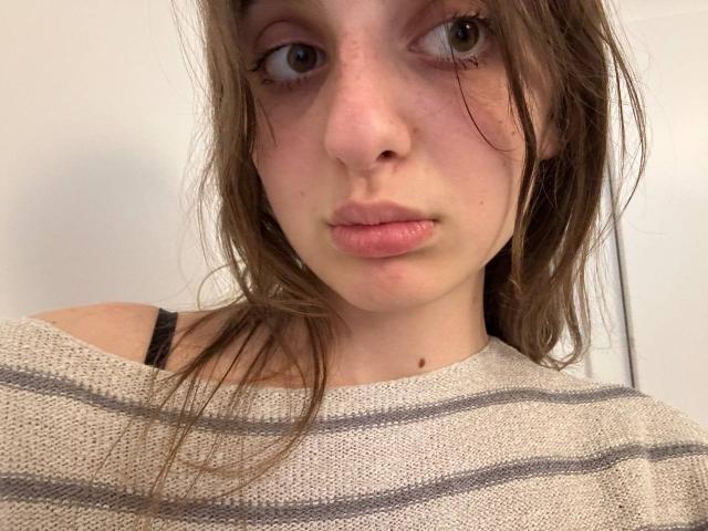 KarieMestler has puffy pink lips, slightly freckled pale skin, brown eyes, and messy brown hair. She's wearing a striped beige sweater with black straps.