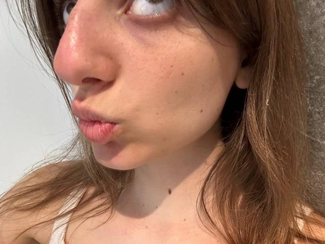 KarieMestler's face, showing her nose, pouty lips, and brown hair, with a small mole on her chin, and freckles on her fair skin. Her eyes look slightly upward.