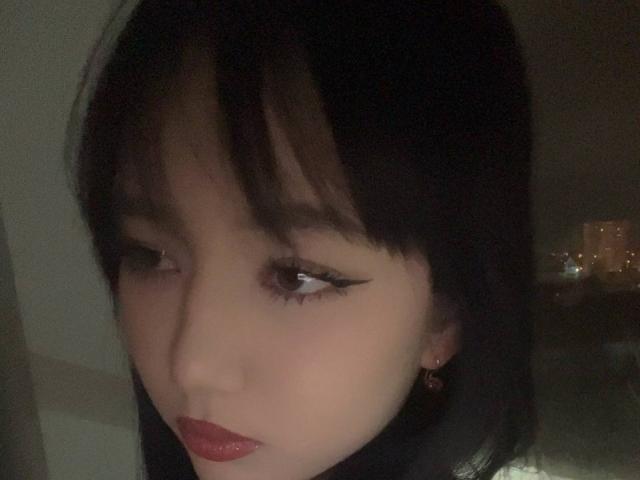 MargeretEskuchen has pale skin, black straight hair with bangs, dark eyeliner, and red lipstick, looking slightly to the side with a serious expression.