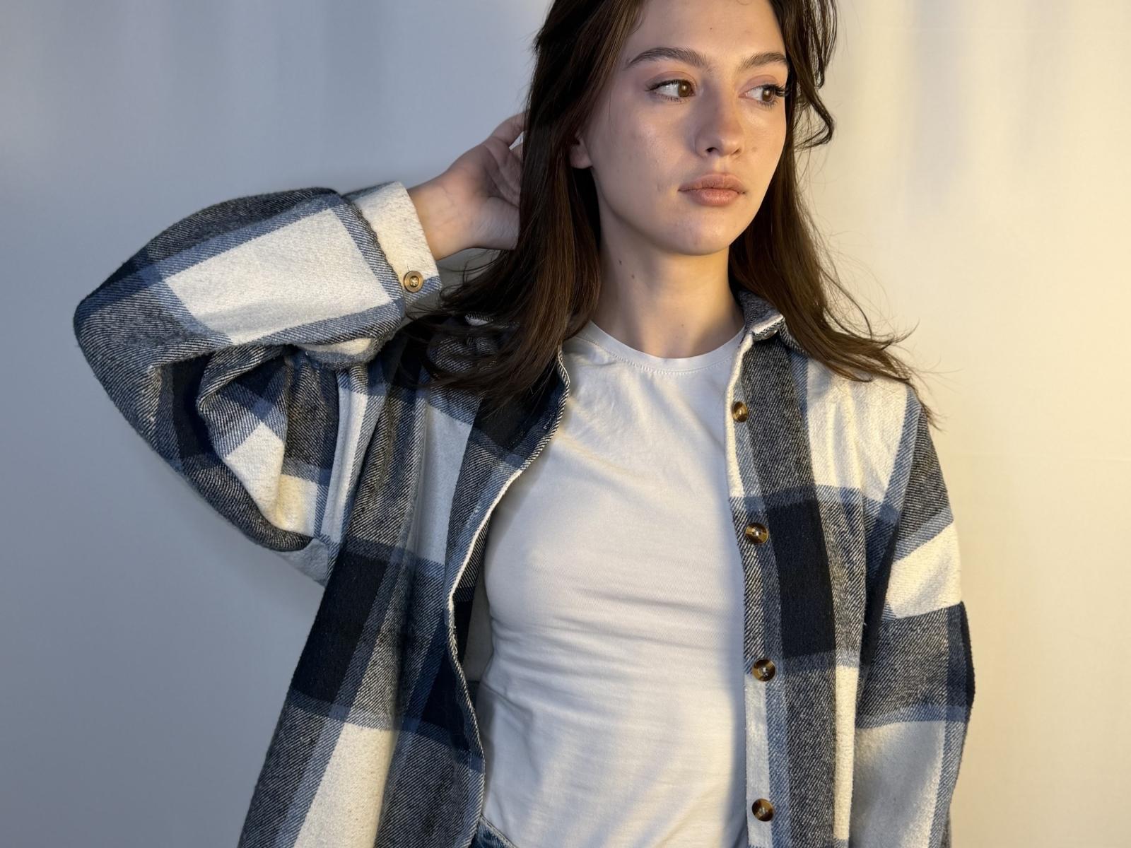 DanicaStuer with brown hair, wearing a white tee and blue-gray plaid shirt, hand in hair, serious expression, soft lighting.