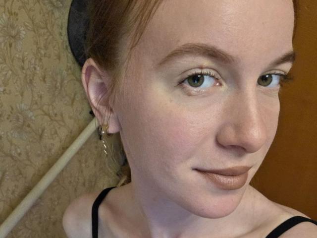 DebbyPennimpede a une peau pâle, des yeux verts clairs et du maquillage marron sur les lèvres. Elle porte un haut noir, avec une casquette noire et des boucles d'oreilles pendantes..