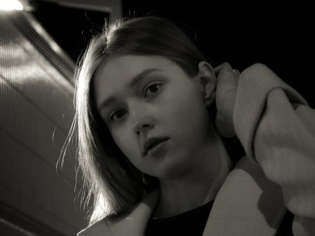 Black-and-white photo of MaryaGruen with light brown hair, looking slightly down, wearing a hoodie, hand in hair, soft light from the left, subtle shadow on right side.