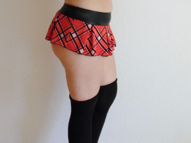 Ein rothaariges Mädchen mit nacktem Hintern in einem roten Karorock, kombiniert mit einem schwarzen Oberteil und schwarzen, hohen Strümpfen, die helle Haut und einen schlanken, attraktiven Körper zeigen..